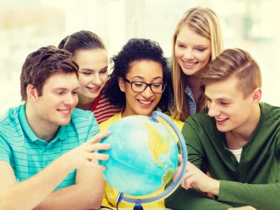 five smiling student looking at globe at school